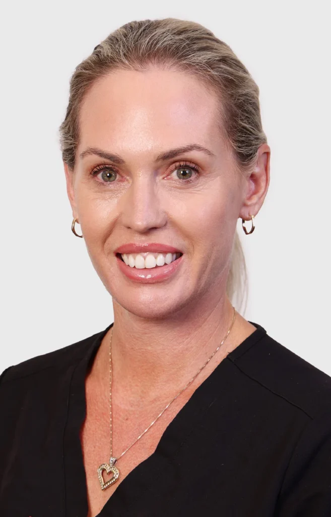 Teneale-nurse - Anue Professional headshot of a smiling woman with blonde hair tied back, wearing a black top and a heart pendant necklace.