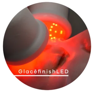 Close-up of a red LED light therapy device applied to a closed eye during a facial treatment; gray rounded head near the eye.