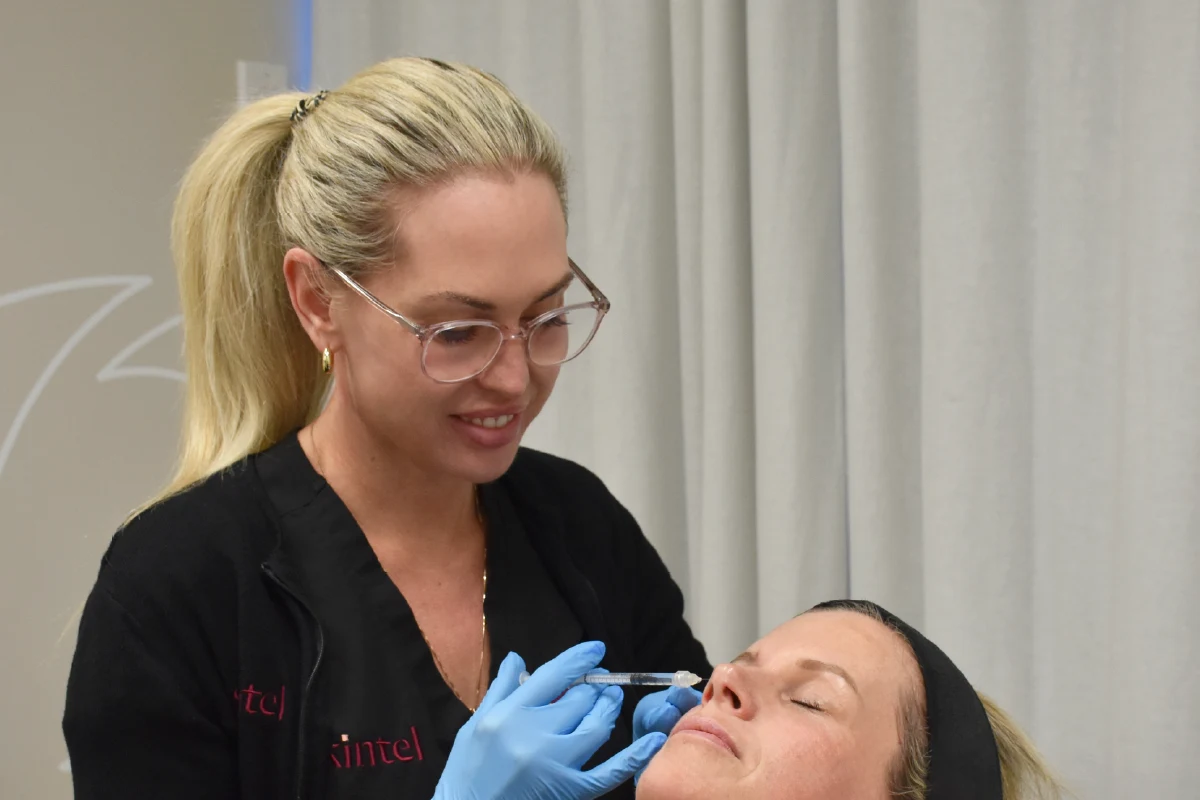 shine-teneale - Anue Esthetician in glasses and gloves administering a facial treatment to a client with eyes closed in a clinical setting